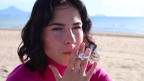 Young Woman Smokes a Cigarette on the Beach Close Up