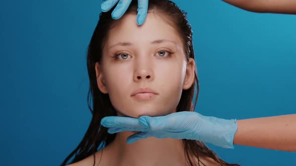 Plastic Surgeon Checking and Measuring Woman Face Before Operation on Blue Background alt