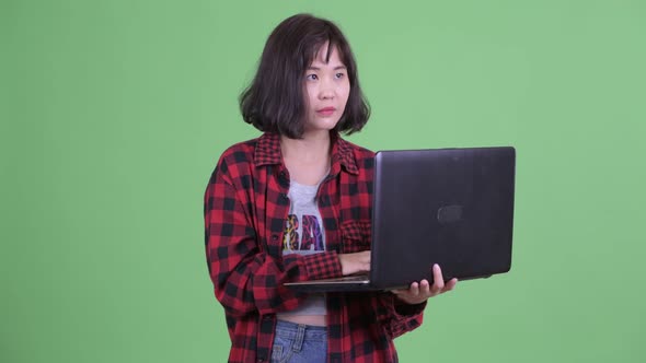 Happy Asian Hipster Woman Thinking While Using Laptop alt