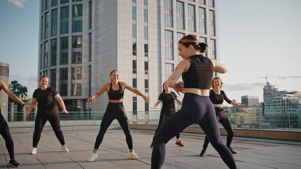 Women Dancing Zumba in the City Square Together with a Young Female Trainer alt