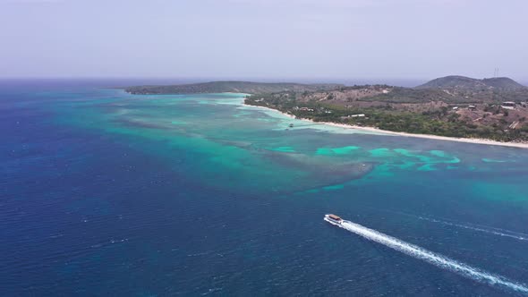 Tourist boat navigates in blue sea along Playa Ensenada beach in Dominican Republic. Aerial drone vi alt