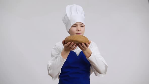 Satisfied Male Little Baker Smelling Delicious Bread Stretching Pastry to Camera Smiling alt