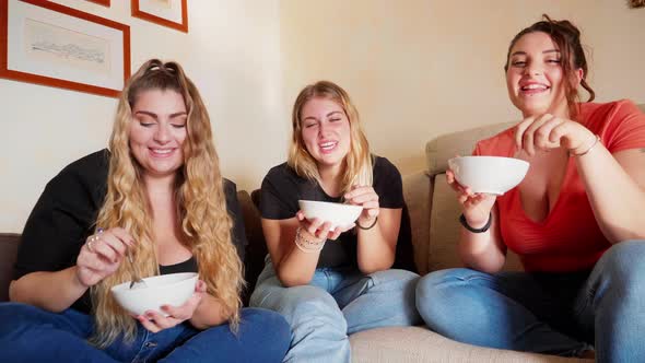 Three young women smiling to camera and eating fruit salad from bowls, Italy