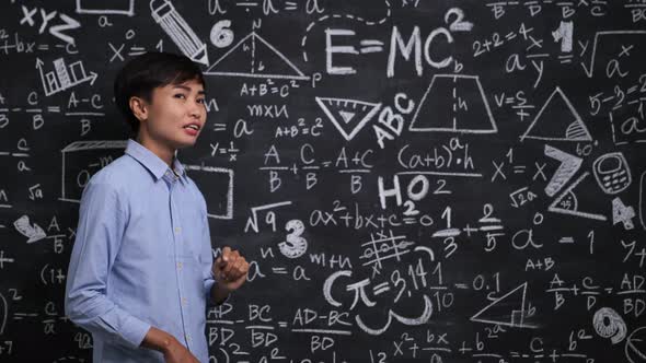 Portrait of smiling asian woman math teacher set against a blackboard in a school classroom alt
