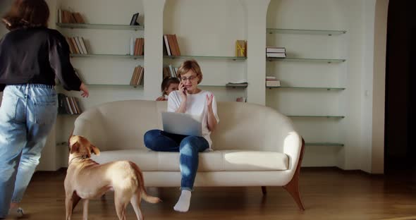 Tired Wife Sitting on the Couch Annoyed While a Noisy Little Daughter Screams Jumps on the Couch and alt