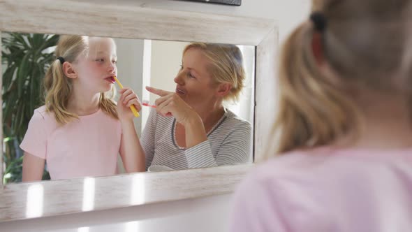 Over the shoulder view of Caucasian woman and her daughter brushing their teeth alt