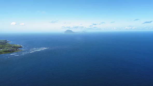 Aerial shot of blue sea, an island with a settlement and shadow of mountain in Saint Kitts and Nevis alt