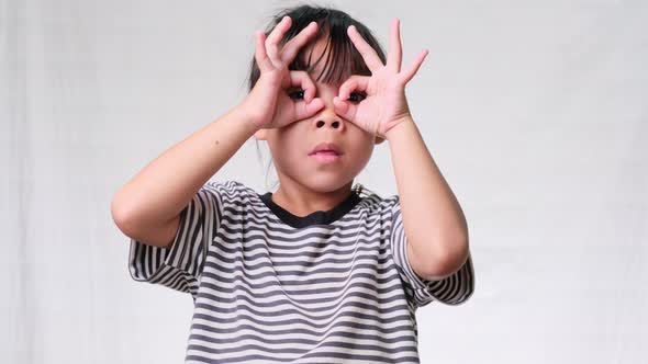 Cute little girl making okay gesture with hands on eyes and looking through fingers over alt