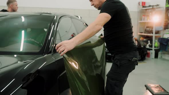 Men are Vinyl Wrapping a Car in a Work Studio Pasting Vinyl Film on a Car