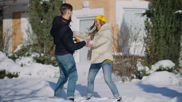 Wide Shot of Funny Couple Dancing in Snow on Winter Backyard alt