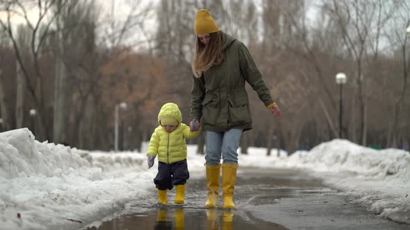 Mom and Daughter Walking in a Puddle in Yellow Rubber Boots