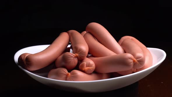 Sausages spinning on a white plate on a black background. alt