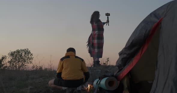 Young Traveler Couple Making Selfie on the Top of Hill at Background of Campfire and Tent in Evening