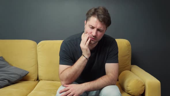 Unshaven Guy Sits on Sofa and Suffers From Toothache