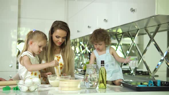 Mother With Daughters Cooking Food In Modern Light Kitchen alt