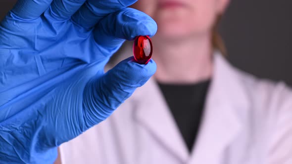 Close-up of Woman in Medical Gloves Holding a Red Pill, the Covid-19 Pandemic alt