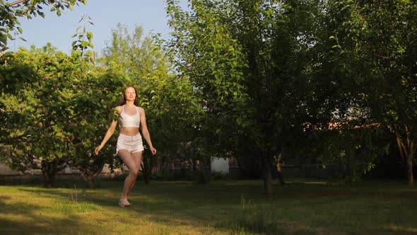 Attractive Young Woman Running and Dancing in the Green Summer Garden
