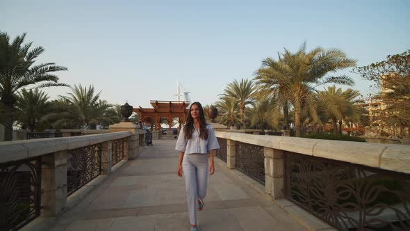 Woman Walking Across the Bridge in Dubai with Burj Al Arab in the Background alt