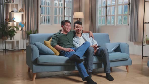 Happy Asian Gay Couple Watching Tv While Sitting On A Couch In Home, Watching Funny Videos alt