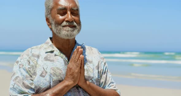 Front view of active senior African American man performing yoga on the beach 4k alt