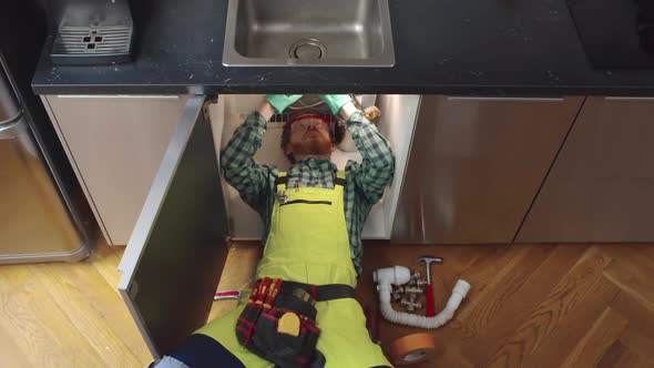 Top View of Handyman Lying Down Under the Sink to Repair Pipe in Kitchen alt