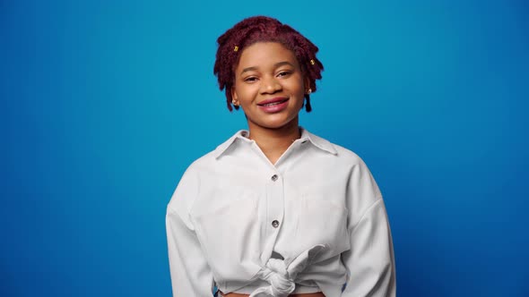 Peaceful Young Afro American Woman in White Shirt Smiling Against Blue Background