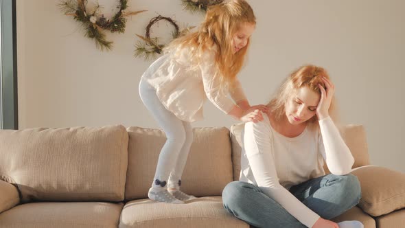 Mindful single mother sitting on sofa while active energetic child daughter bothers young mom at hom