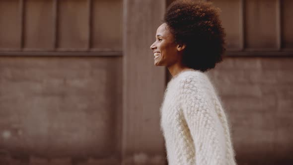 Smiling Young Woman With Windswept Afro Hair Walking Along Street alt