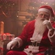 Relaxed Santa Claus Is Sitting in Living Room with Christmas Decorations and Tree, Looking at Camera - VideoHive Item for Sale