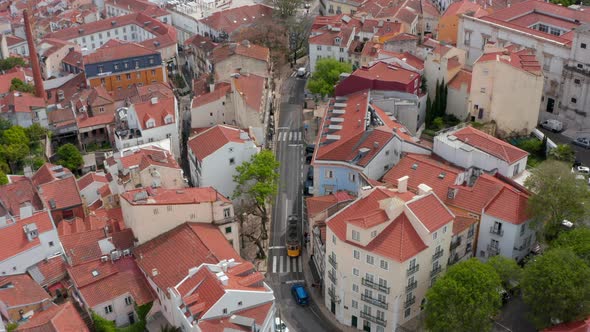 Aerial Overhead Top Down View of Yellow Tram Driving on the Tracks Through Narrow Residential alt