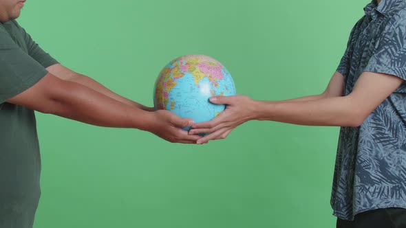 Man Hand In The World Globe To Another Man While Standing In Front Of Green Screen Background alt