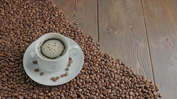 Black Coffee in a White Mug with Spinning Bubbles on a Flat Wooden Surface Partially Covered with
