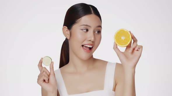 Cute female model clean fresh skin is holding sliced of cucumber and orange. alt