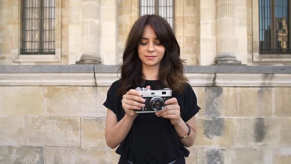 Young Woman Making Photo Rewinding a Film Camera on Background of Old Buildings in Paris