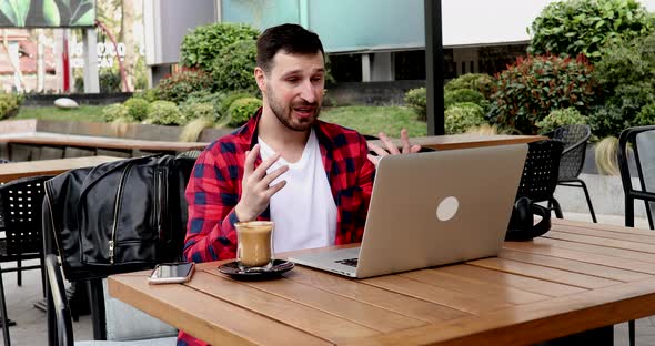 Young man having a video call on laptop while sitting at a cafe.