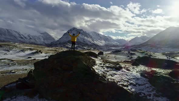 Male Mountain Climber Raising Hands with Icepick on Top of Snowy Peak alt