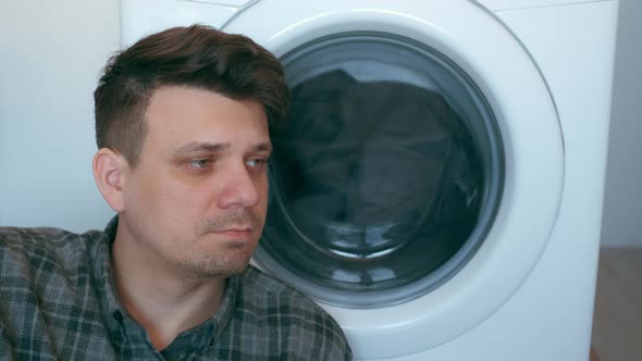 Tired Man is Waiting the Washing Machine with Grey Bedspread Inside It