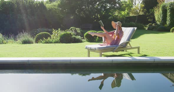 Caucasian woman reading a book while sunbathing on a deck chair in the garden alt