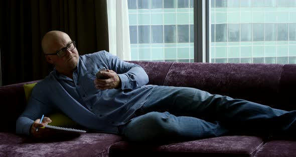 Freelancer Man Is Lying on Couch and Thinking, Reading Site on Cell Phone By Internet alt