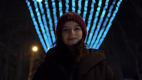 Attractive Woman Walking on Street at Winter Night Looking at Camera Smiling