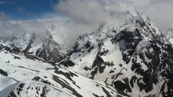 Air Flight Through Mountain Clouds Over Beautiful Snowcapped Peaks of Mountains and Glaciers alt