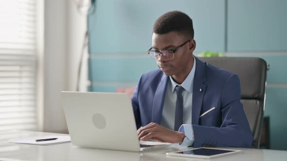 Young African Businessman Looking at Camera While Using Laptop in Office alt