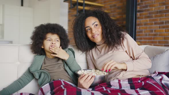 Young Attractive Woman and Her Little Son are Sitting on the Sofa and Watching TV alt
