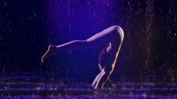 Sporty Woman Stands in Advanced Headstand with Studio Blue Light and Water Rain. Female Body in alt