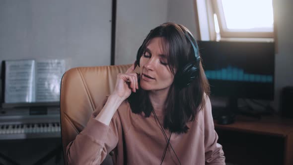 A beautiful girl with headphones listens to music in a chair at the computer and sings, smiles. Slow