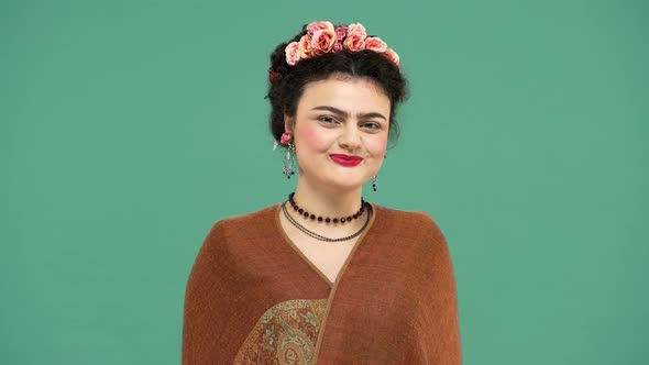 Studio Portrait of Frida Kahlo Lookalike Woman in Mexican Dress Wearing Jewelry and Roses in Hair alt