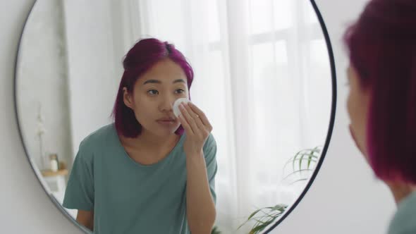 Young Asian Woman Applying Lotion to Face with Cotton Pad alt