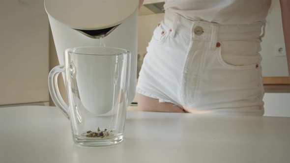 A Young Woman is Pouring Water Into a Cup From a Teapot alt