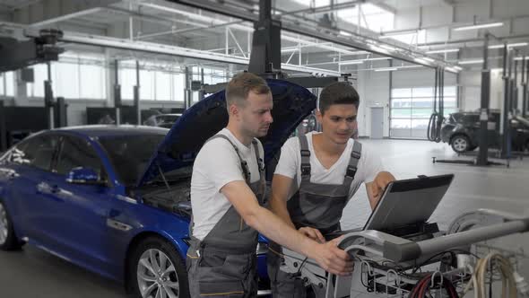 Mature Mechanic and His Assistant Using Computer at Car Repair Station alt