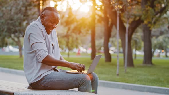 Cheerful Carefree Senior Black Man Sitting Outdoor Using Laptop Plays Having Fun Laughing Pretending alt
